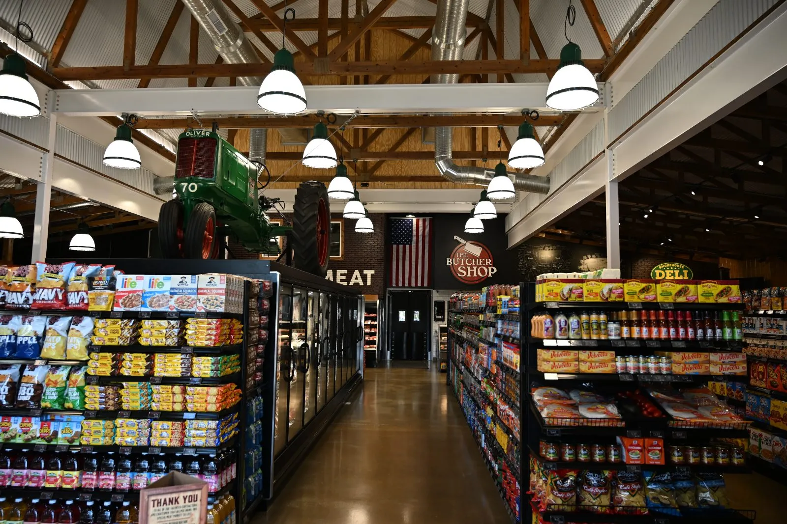 Grocery aisles at Farm Country Meats & Market in Union, Missouri, with packaged goods, a cooler case, and a vintage tractor hanging above the butcher shop sign.